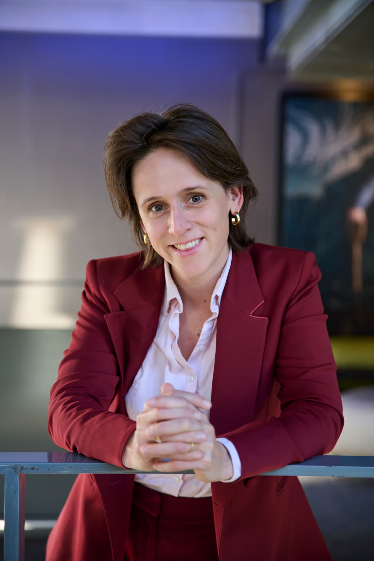 Margaux Pelen in a burgundy blazer, leaning on a railing and looking at the camera